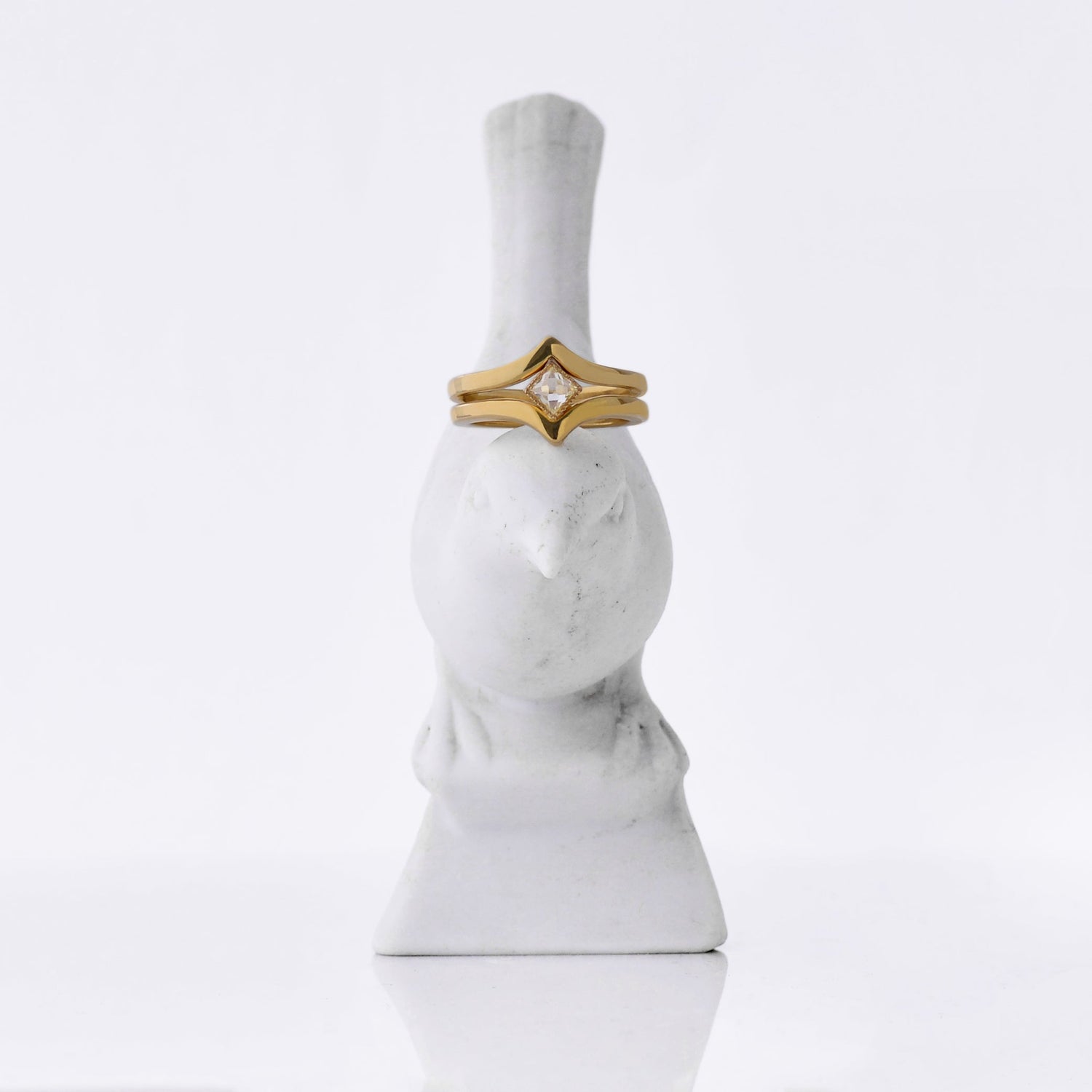 2 rings made from 18kt Fairmined yellow gold, the top one has a bezel set square rose-cut diamond. They are stacked on a porcelain bird sculpture.