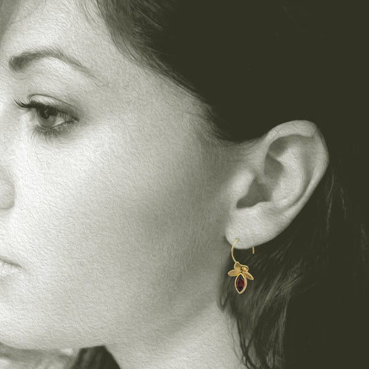 14kt yellow gold earrings with a 3 leaf design have 2 bezel set,  5mm x 7mm marquise cut responsibly sourced dark red Rhodolite Garnets. Earrings are 1.25" long with a french style ear wire. Shown on model.