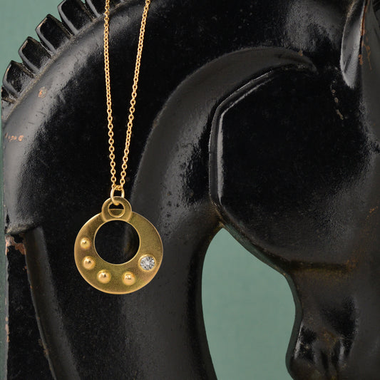 The Circle Shield Motif that you wear over your heart helps you visualize your inner strength that gives you your personal power.
Hand Fabricated in 18kt recycled yellow gold and a round white 3.5mm reclaimed diamond, the CIRCLE SHIELD Pendant encourages us to savor the important moments and gently reminds us that we own our power, no one else.
The Circle Shield Pendant is handcrafted in Minnesota from 18kt yellow gold recycled in studio forged from retired jewelry.  