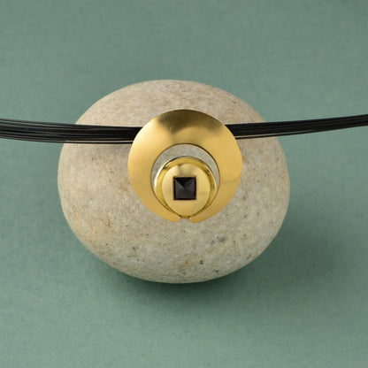 The Moon Pendant has a 4mm genuine square cut Black Spinel gemstone and the multiple circle dome shaped pieces make up the pendant . it is approximately 1" in diameter and hangs from a 17” multi strand black ruthenium plated sterling silver collar with a 14kt gold barrel clasp.