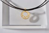 1" round pendant with small holes as the design. In some holes there are small diamonds flush set. Made of 18kt Fairmined yellow gold, and it is on a 17" multi strand leather neck cord with an 18kt yellow gold clasp.